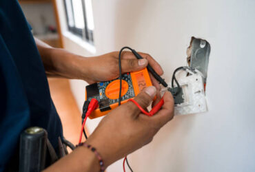 Close-up on an electrician fixing an electrical outlet and measuring the voltage at a house - home improvement concepts