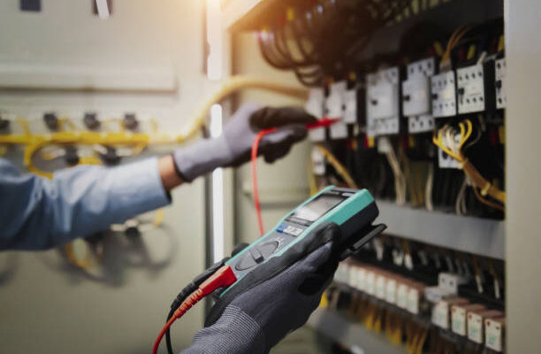 Electricity and electrical maintenance service, Engineer hand holding AC multimeter checking electric current voltage at circuit breaker terminal and cable wiring main power distribution board.